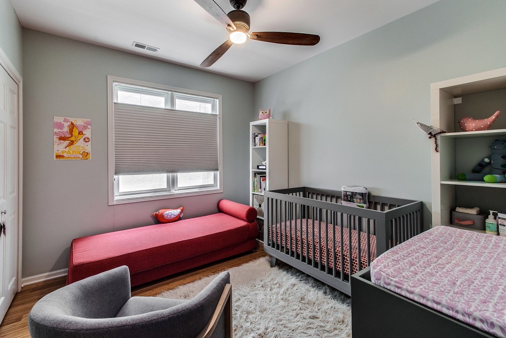 Modelo de habitación de bebé neutra actual de tamaño medio con paredes grises y suelo de madera en tonos medios