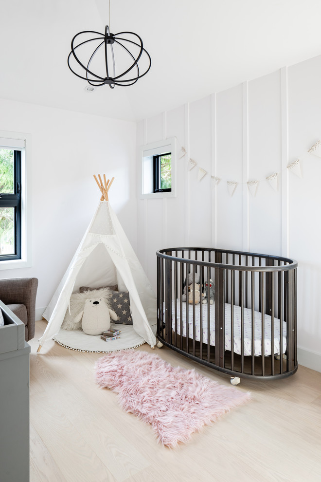 Réalisation d'une chambre de bébé fille nordique avec un mur blanc, parquet clair et un sol beige.