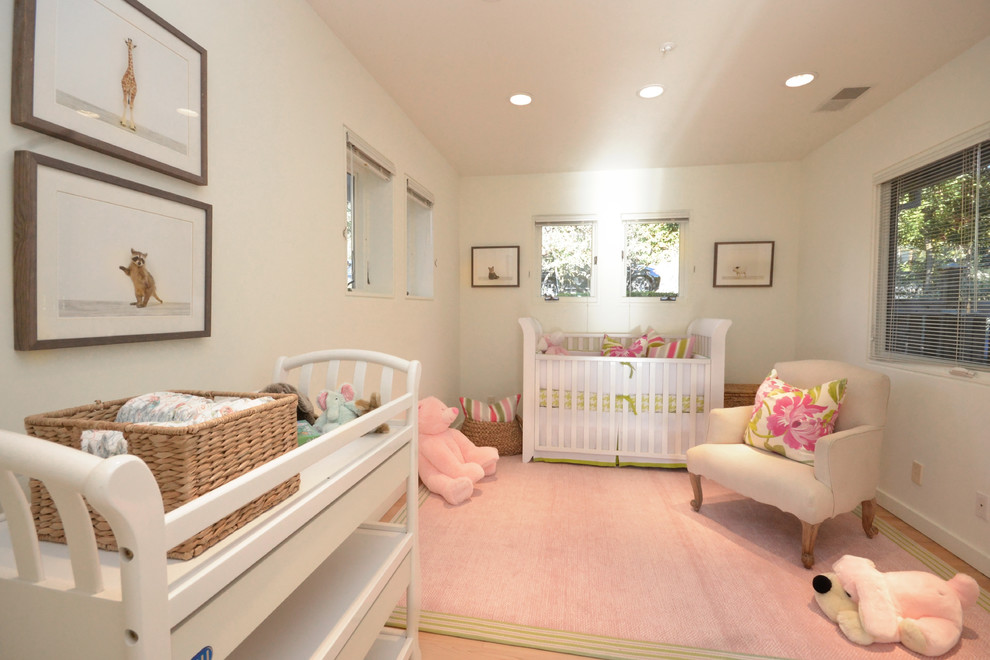 Ejemplo de habitación de bebé niña clásica con paredes blancas, suelo de madera clara y suelo rosa