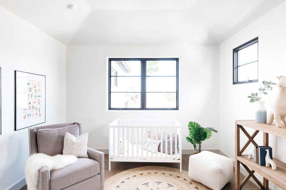 Modelo de habitación de bebé mediterránea con paredes blancas, suelo de madera en tonos medios y suelo marrón