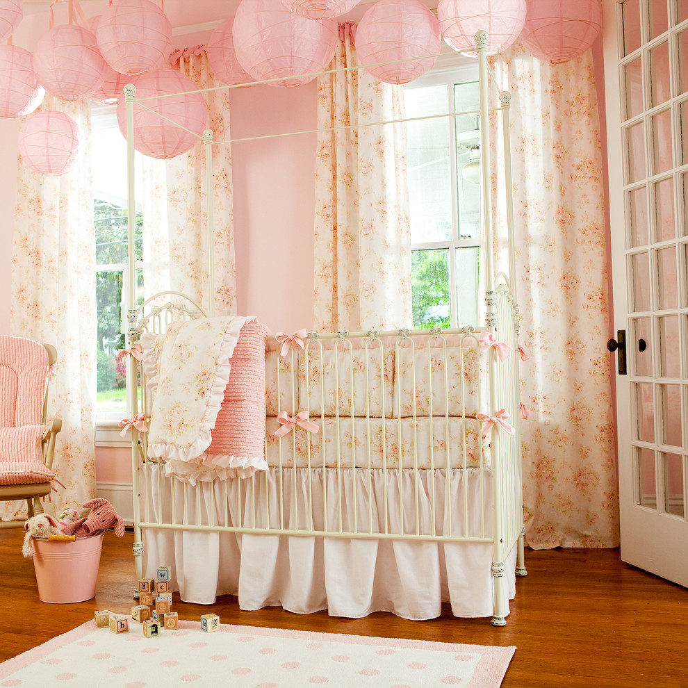 Imagen de habitación de bebé niña romántica con paredes rosas, suelo de madera en tonos medios y suelo naranja