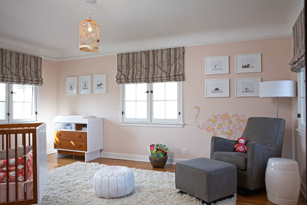 Immagine di una cameretta per neonata chic con pareti rosa e pavimento in legno massello medio