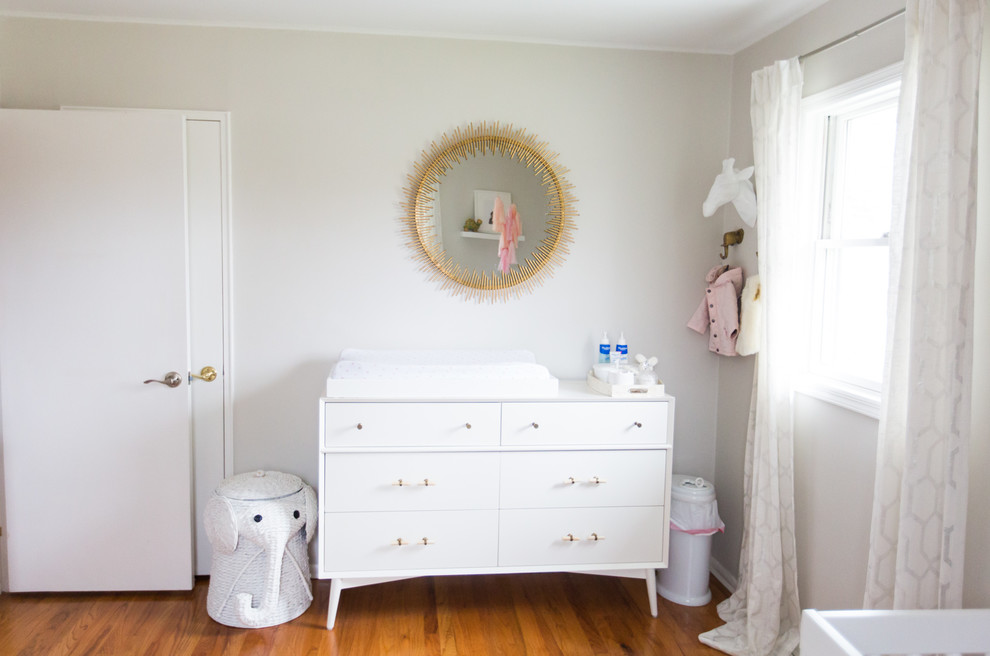 Imagen de habitación de bebé niña moderna de tamaño medio con paredes grises y suelo de madera en tonos medios