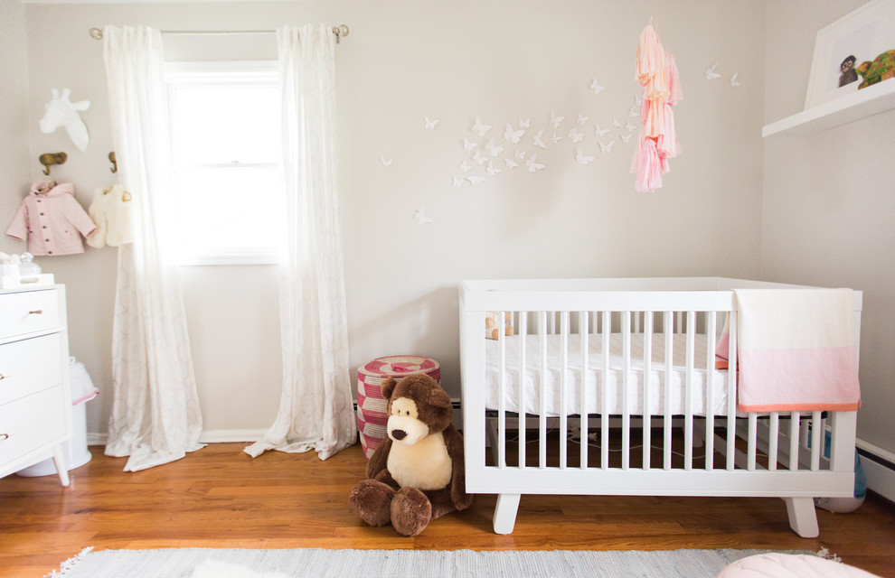 Diseño de habitación de bebé niña moderna de tamaño medio con paredes grises y suelo de madera en tonos medios