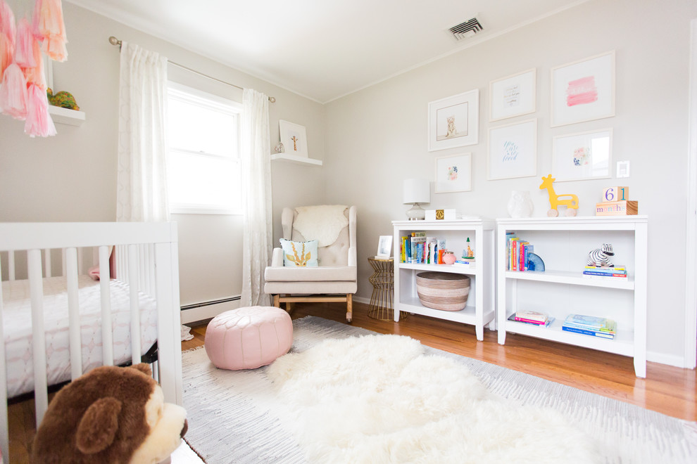 Design ideas for a medium sized modern nursery for girls in New York with grey walls and medium hardwood flooring.