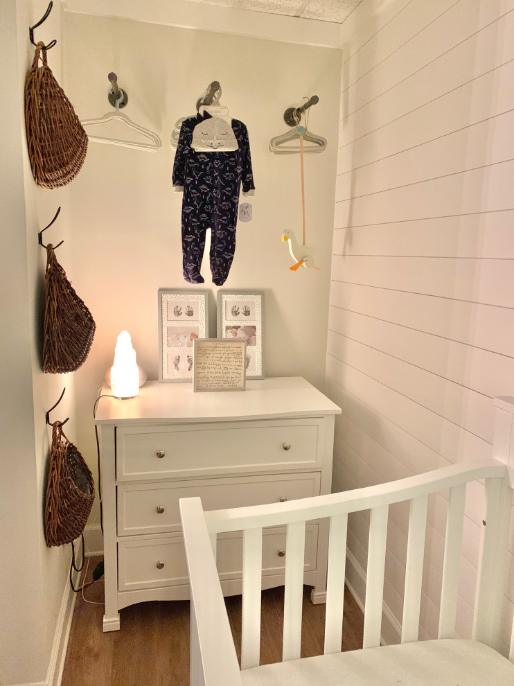 Imagen de habitación de bebé neutra de estilo de casa de campo pequeña con paredes blancas, suelo vinílico, suelo beige y machihembrado