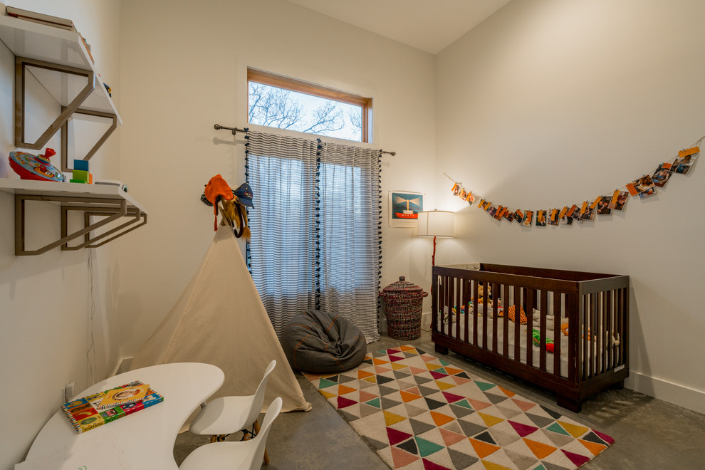 Ejemplo de habitación de bebé neutra contemporánea con paredes blancas y suelo de cemento