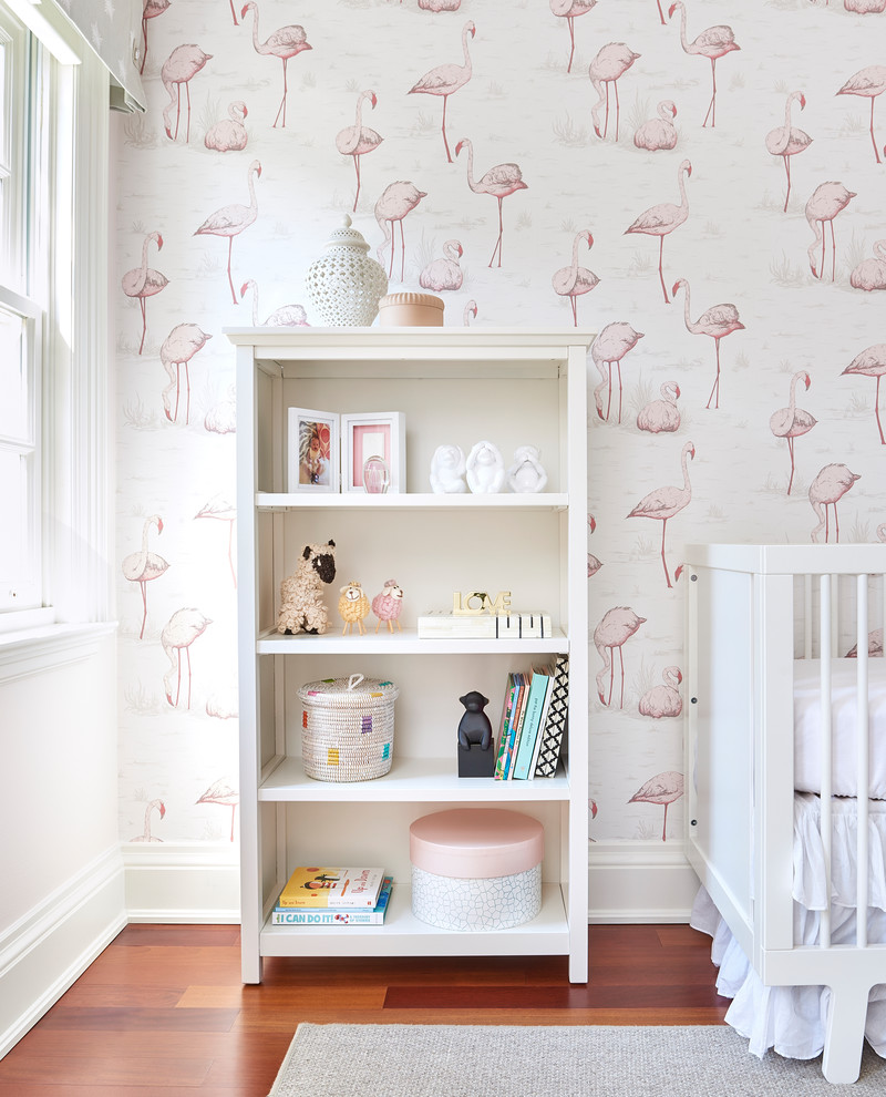 Modelo de habitación de bebé niña clásica renovada de tamaño medio con paredes rosas, suelo de madera en tonos medios y suelo marrón