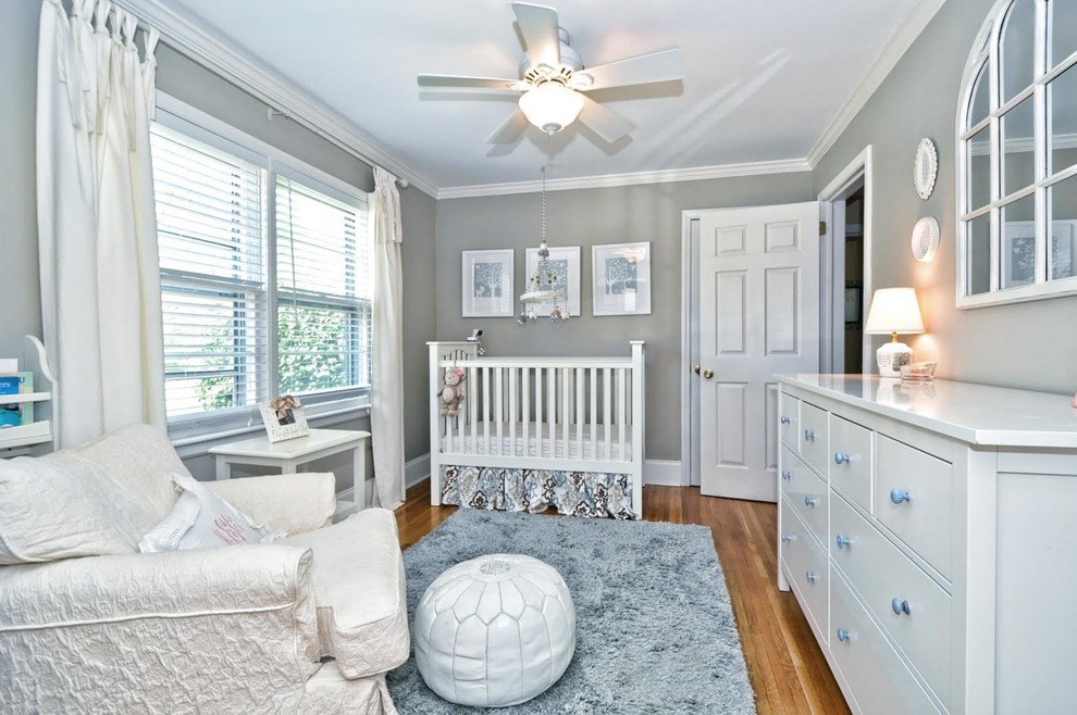 Modelo de habitación de bebé neutra clásica con paredes grises y suelo de madera en tonos medios