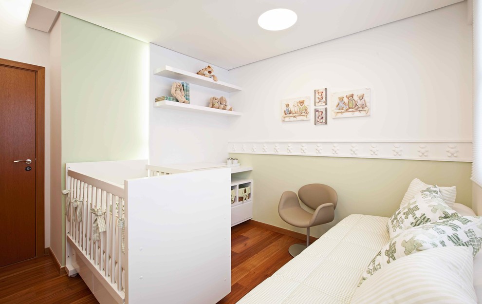 Cette photo montre une chambre de bébé neutre tendance avec un mur vert et un sol en bois brun.