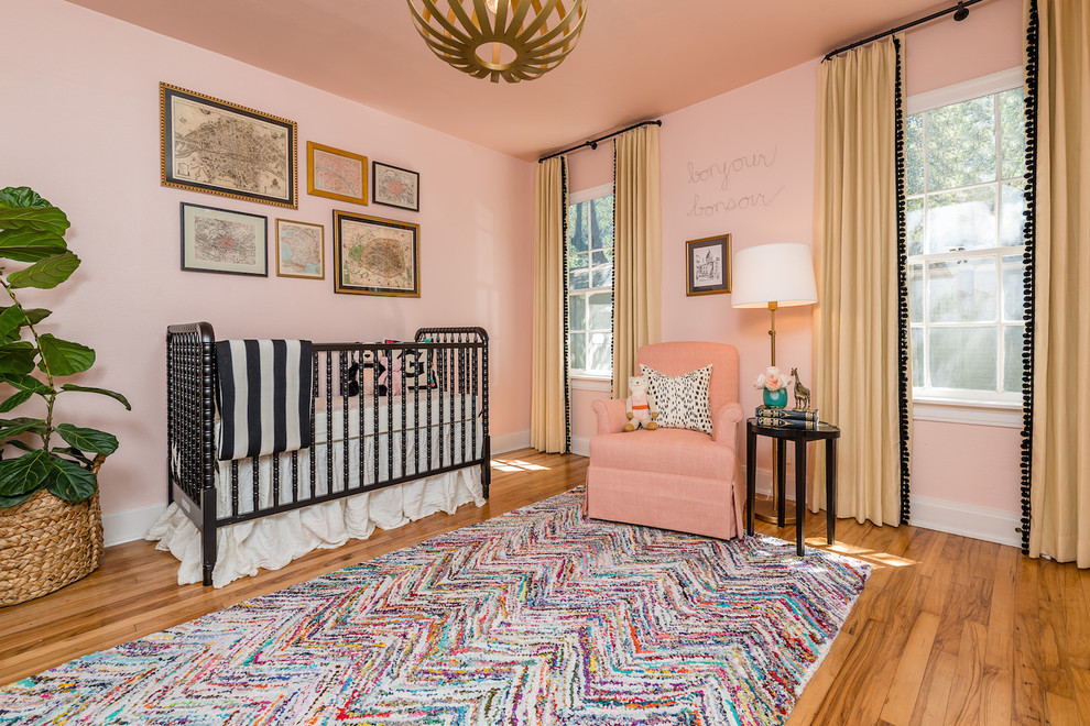 Cette photo montre une chambre de bébé fille chic avec un mur rose, un sol en bois brun et un sol marron.