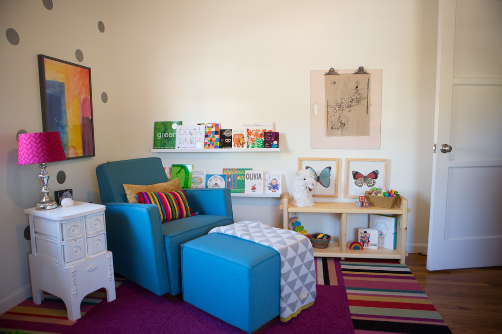 Imagen de habitación de bebé niña ecléctica de tamaño medio con paredes blancas y suelo de madera en tonos medios