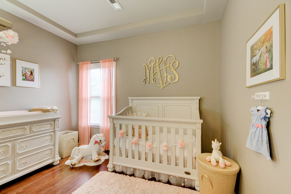Imagen de habitación de bebé niña romántica pequeña con paredes grises, suelo de madera en tonos medios y suelo marrón