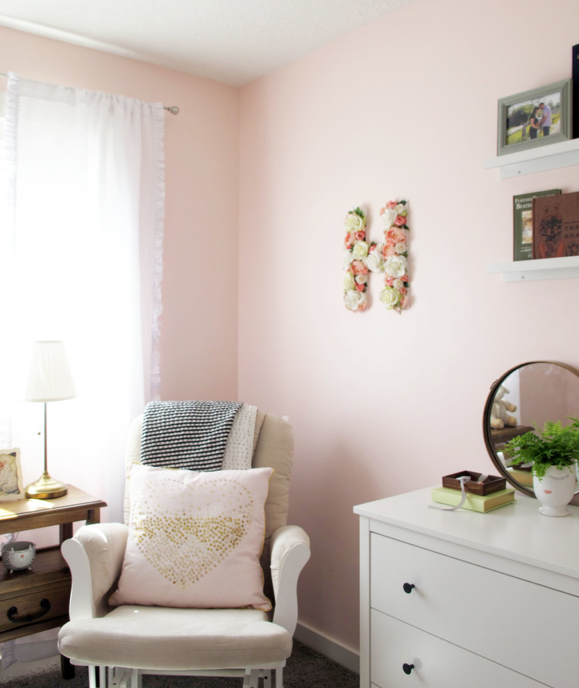 This is an example of a small traditional nursery for girls in Calgary with pink walls, carpet and grey floors.