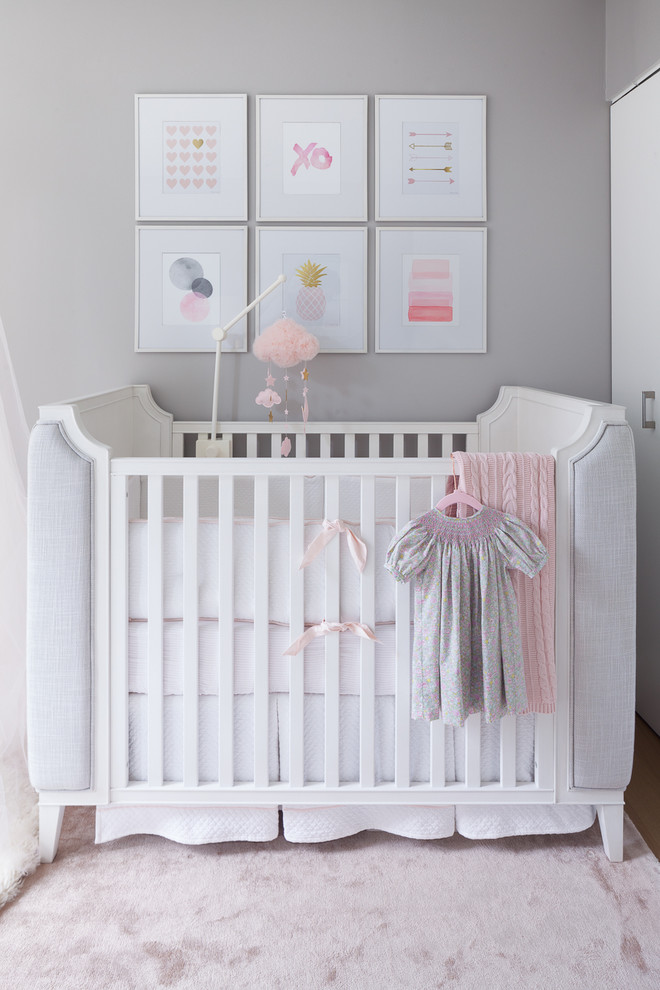Modelo de habitación de bebé niña tradicional renovada pequeña con paredes grises, moqueta y suelo rosa