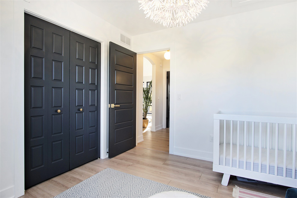 Diseño de habitación de bebé niña escandinava de tamaño medio con paredes blancas, suelo de madera clara y suelo beige