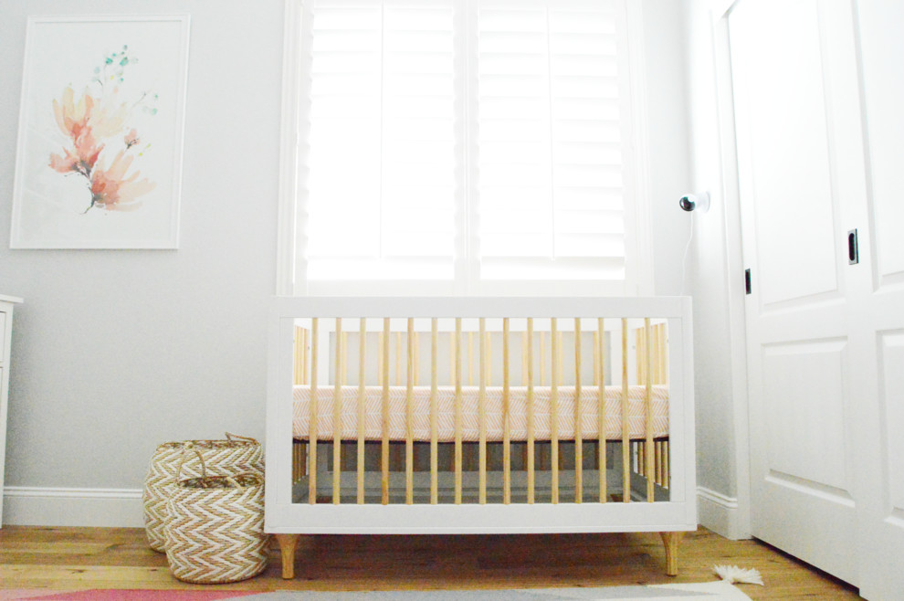Cette photo montre une chambre de bébé fille chic de taille moyenne avec un mur gris et un sol en bois brun.