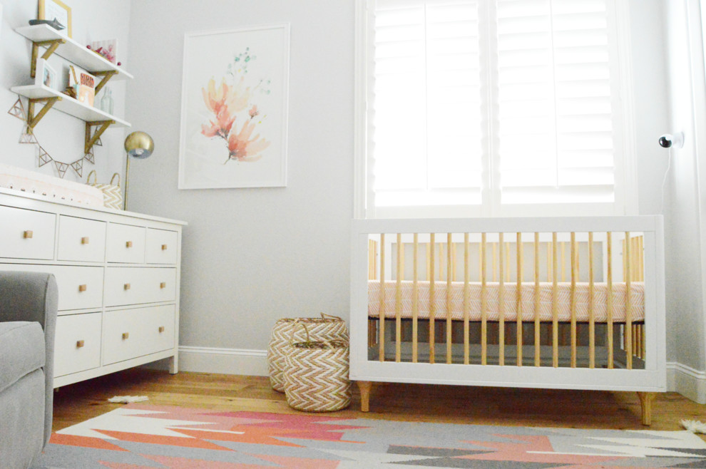 Ejemplo de habitación de bebé niña clásica renovada de tamaño medio con paredes grises y suelo de madera en tonos medios