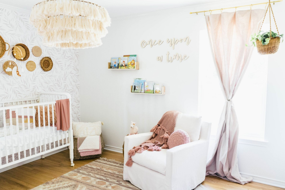 Medium sized country nursery for girls with white walls, light hardwood flooring and brown floors.