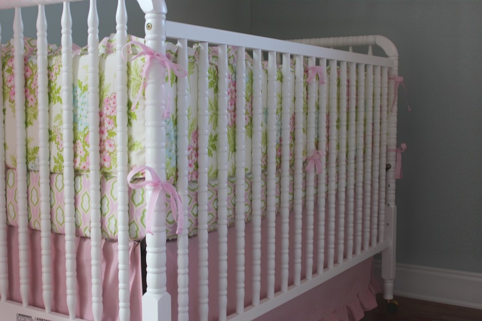 Immagine di una cameretta per neonata tradizionale di medie dimensioni con pareti grigie e pavimento in legno massello medio