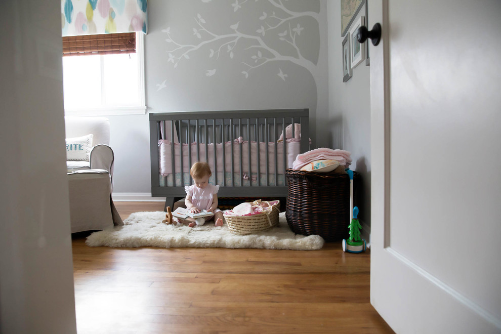 Cette photo montre une petite chambre de bébé fille moderne avec un mur gris et un sol en bois brun.