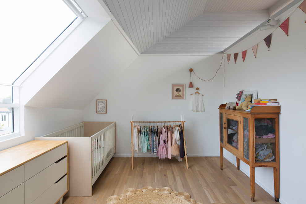 Diseño de habitación de bebé costera con paredes blancas, suelo de madera en tonos medios y suelo marrón