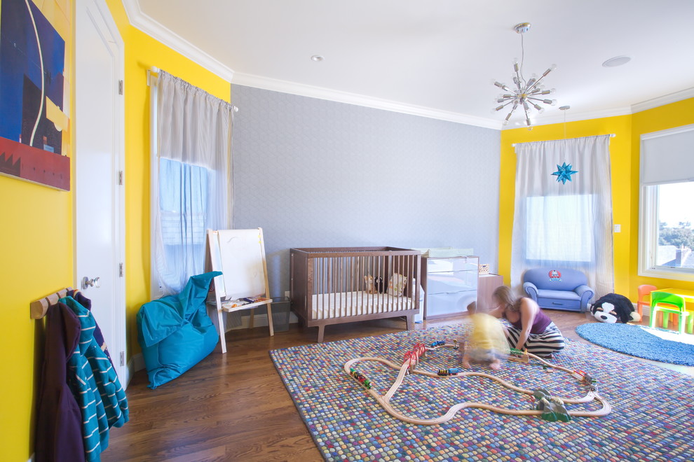 Ejemplo de habitación de bebé neutra actual con paredes amarillas y suelo de madera oscura