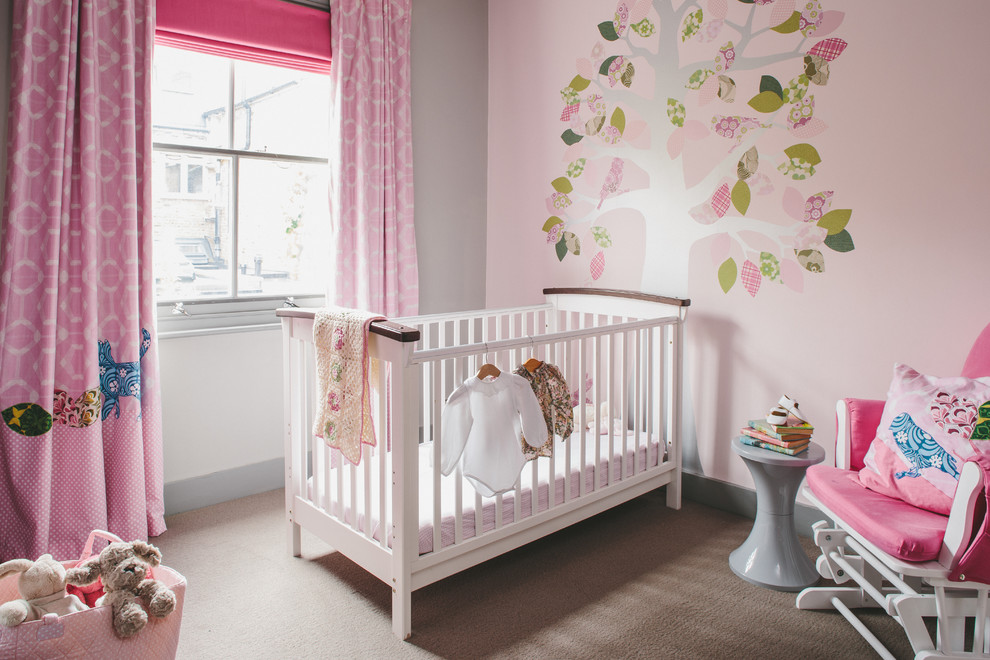 Photo of a traditional nursery for girls in London with pink walls, carpet and brown floors.
