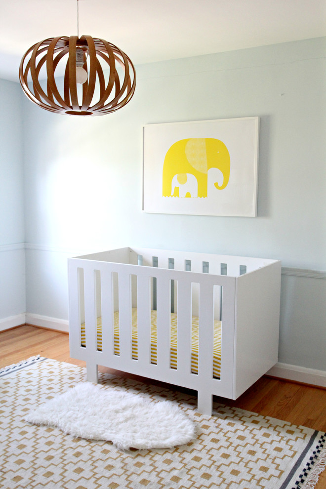 Diseño de habitación de bebé neutra moderna de tamaño medio con paredes azules y suelo de madera en tonos medios