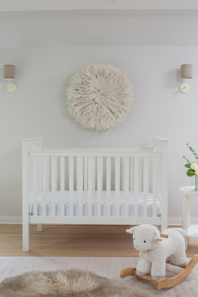 Imagen de habitación de bebé neutra tradicional renovada de tamaño medio con paredes blancas, suelo de madera clara y suelo beige
