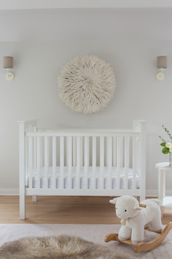 Modelo de habitación de bebé neutra tradicional renovada de tamaño medio con paredes blancas, suelo de madera clara y suelo beige
