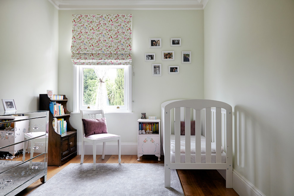 This is an example of a medium sized contemporary nursery for girls in London with green walls and medium hardwood flooring.