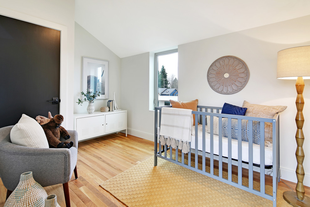 Diseño de habitación de bebé neutra actual grande con paredes blancas, suelo de madera en tonos medios y suelo marrón