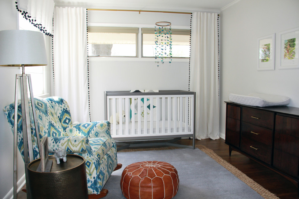 Cette image montre une chambre de bébé neutre minimaliste de taille moyenne avec un mur gris, un sol en bois brun et un sol marron.