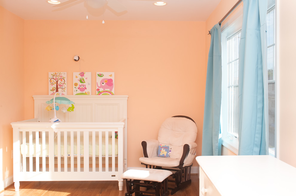 Diseño de habitación de bebé niña clásica de tamaño medio con parades naranjas y suelo de madera en tonos medios