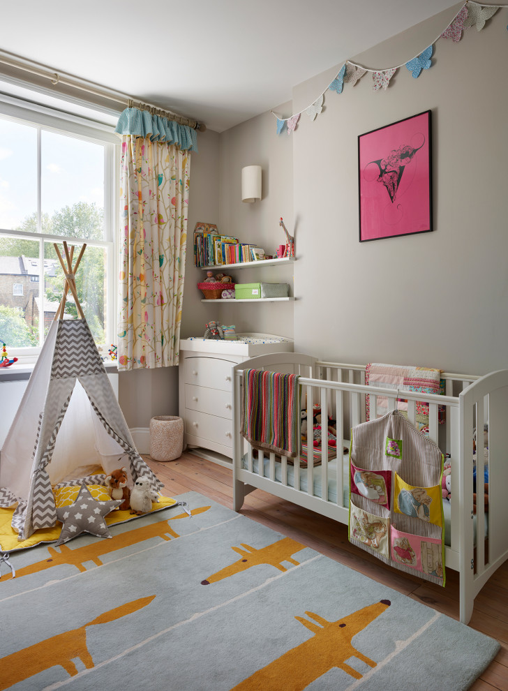 Diseño de habitación de bebé neutra contemporánea con paredes grises y suelo de madera clara