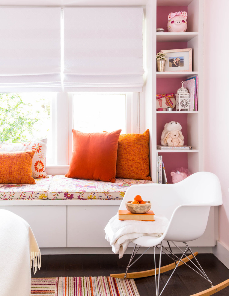 Imagen de habitación de bebé niña actual de tamaño medio con paredes rosas y suelo de madera oscura