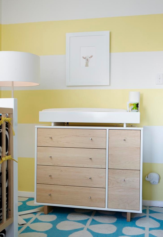 Diseño de habitación de bebé neutra contemporánea con paredes amarillas, suelo de madera en tonos medios y suelo marrón