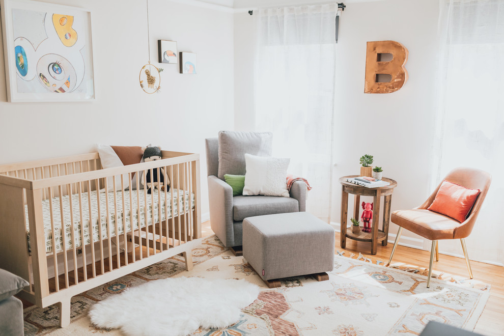 Imagen de habitación de bebé neutra bohemia de tamaño medio con paredes blancas y suelo de madera en tonos medios