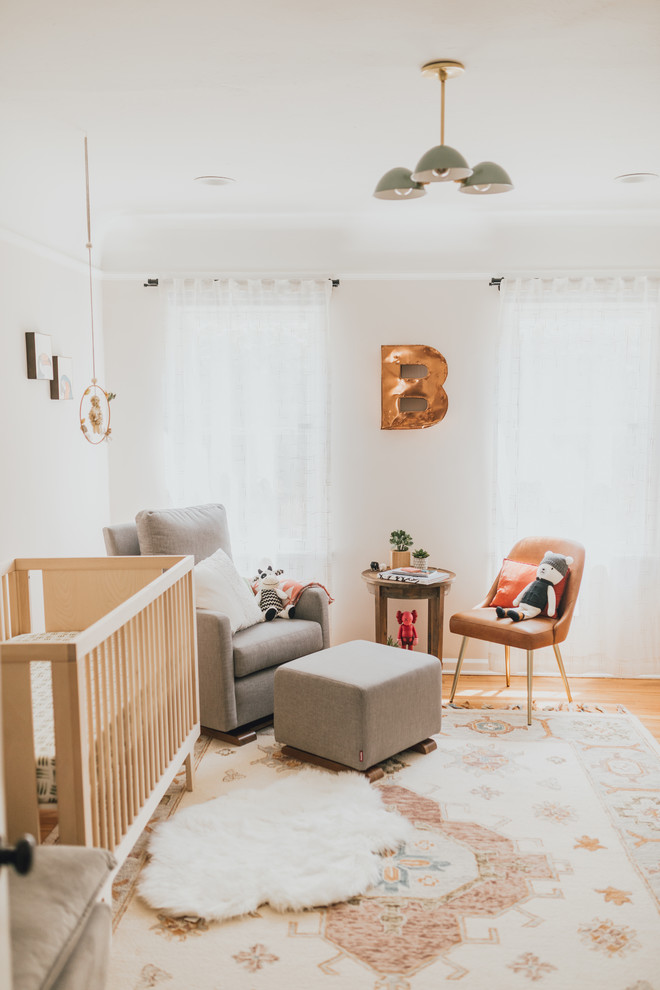 Cette photo montre une chambre de bébé neutre éclectique de taille moyenne avec un mur blanc et un sol en bois brun.