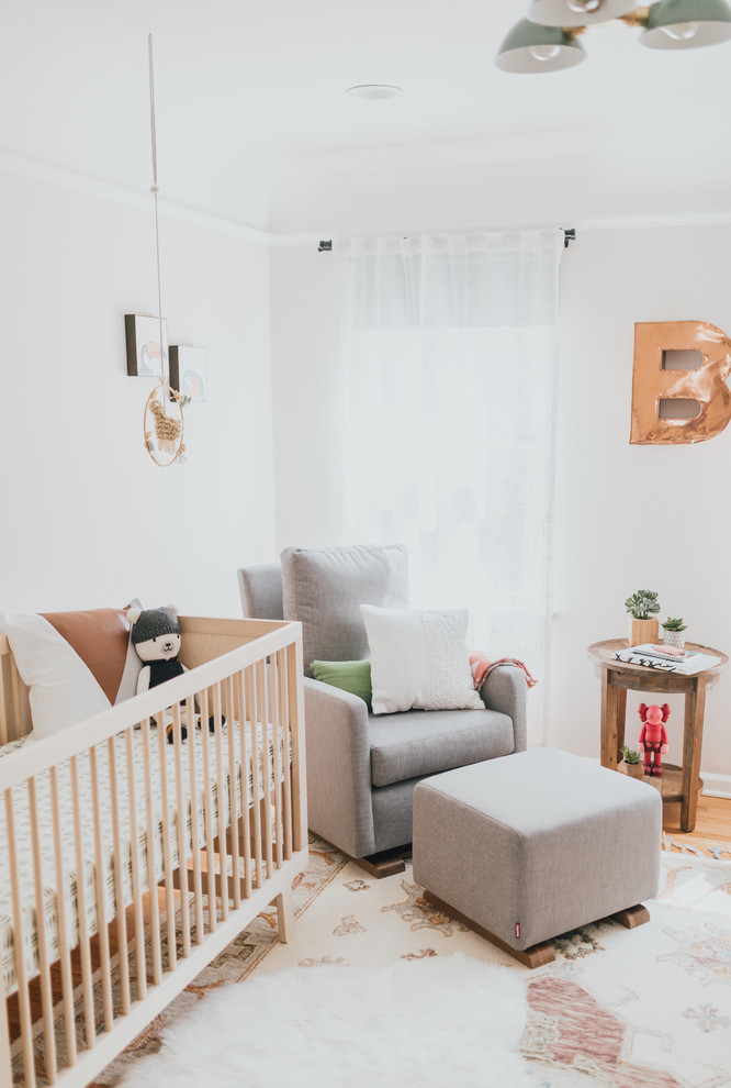 Example of a mid-sized eclectic gender-neutral medium tone wood floor nursery design in Los Angeles with white walls
