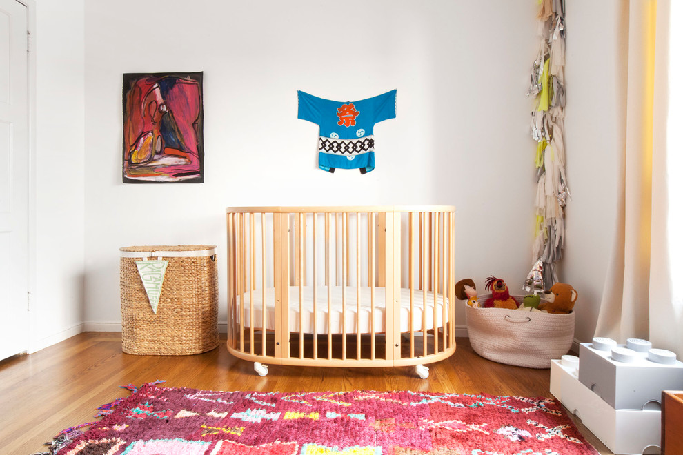 Ejemplo de habitación de bebé neutra ecléctica con paredes blancas y suelo de madera en tonos medios