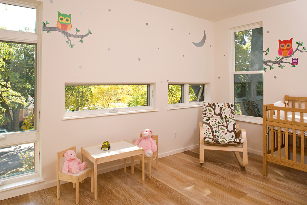 Diseño de habitación de bebé neutra contemporánea con paredes blancas y suelo de madera clara