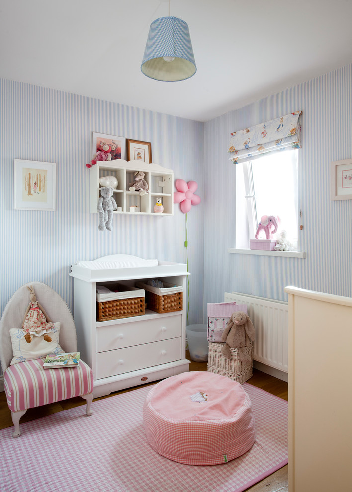 Immagine di una cameretta per neonati neutra chic con pareti blu e pavimento in legno massello medio