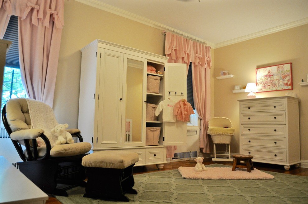 This is an example of a medium sized shabby-chic style nursery for girls in New York with beige walls and light hardwood flooring.