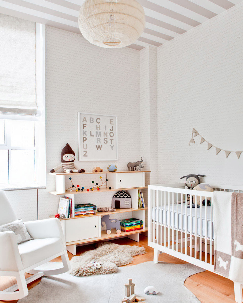 Réalisation d'une chambre de bébé neutre design avec un mur blanc et parquet clair.