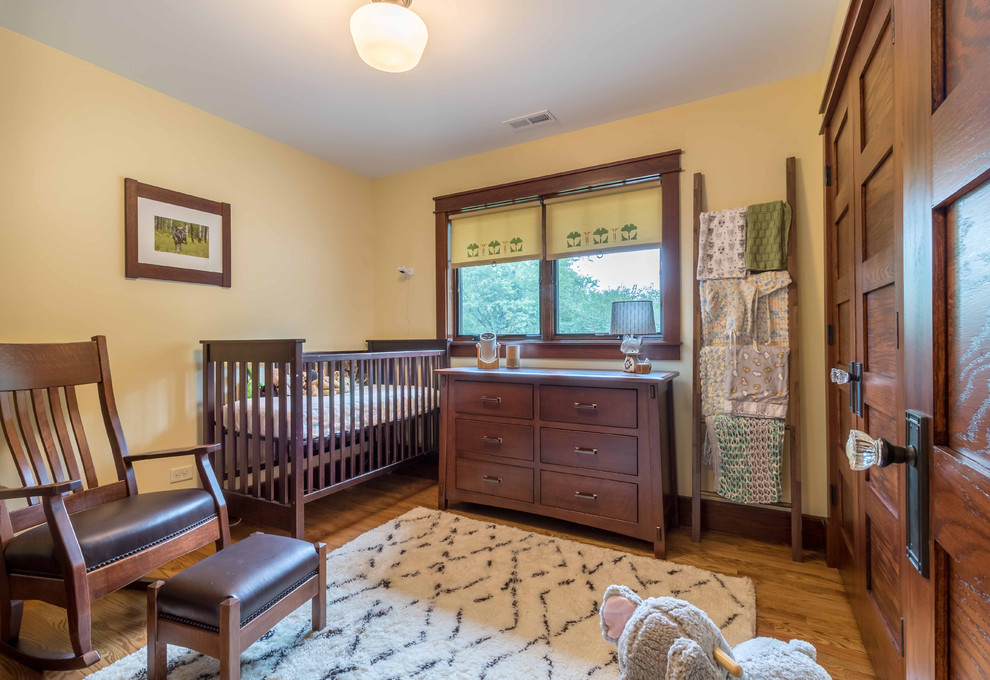 Diseño de habitación de bebé neutra blanca de estilo americano de tamaño medio con paredes amarillas, suelo de madera clara, suelo marrón, papel pintado y papel pintado