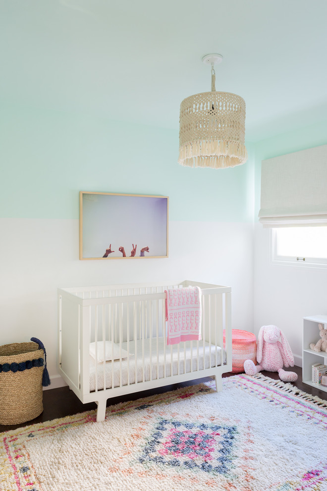 Aménagement d'une chambre de bébé fille bord de mer avec un mur multicolore et parquet foncé.