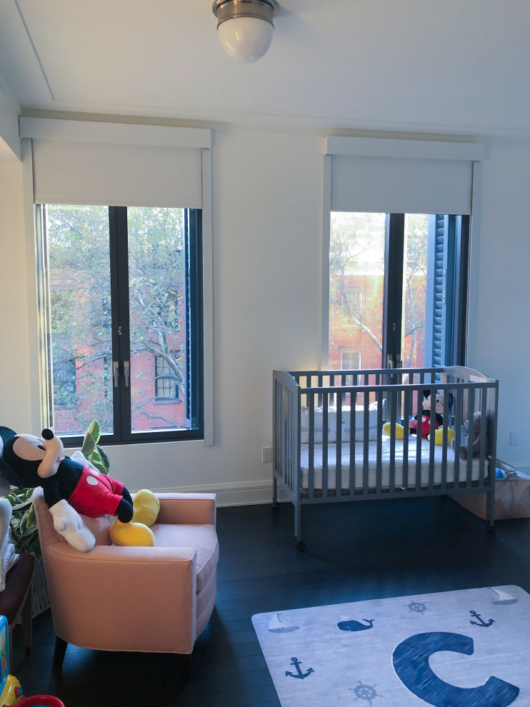Imagen de habitación de bebé neutra grande con paredes blancas, suelo de madera oscura y suelo negro