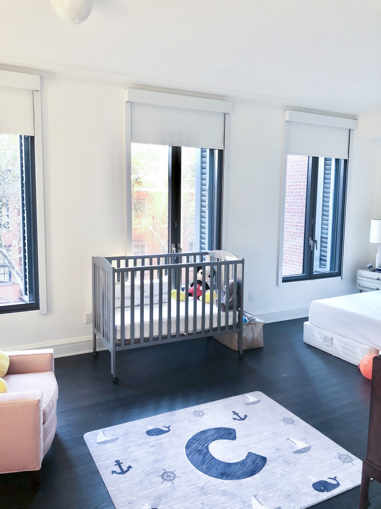 This is an example of a large gender neutral nursery in New York with white walls, dark hardwood flooring and black floors.